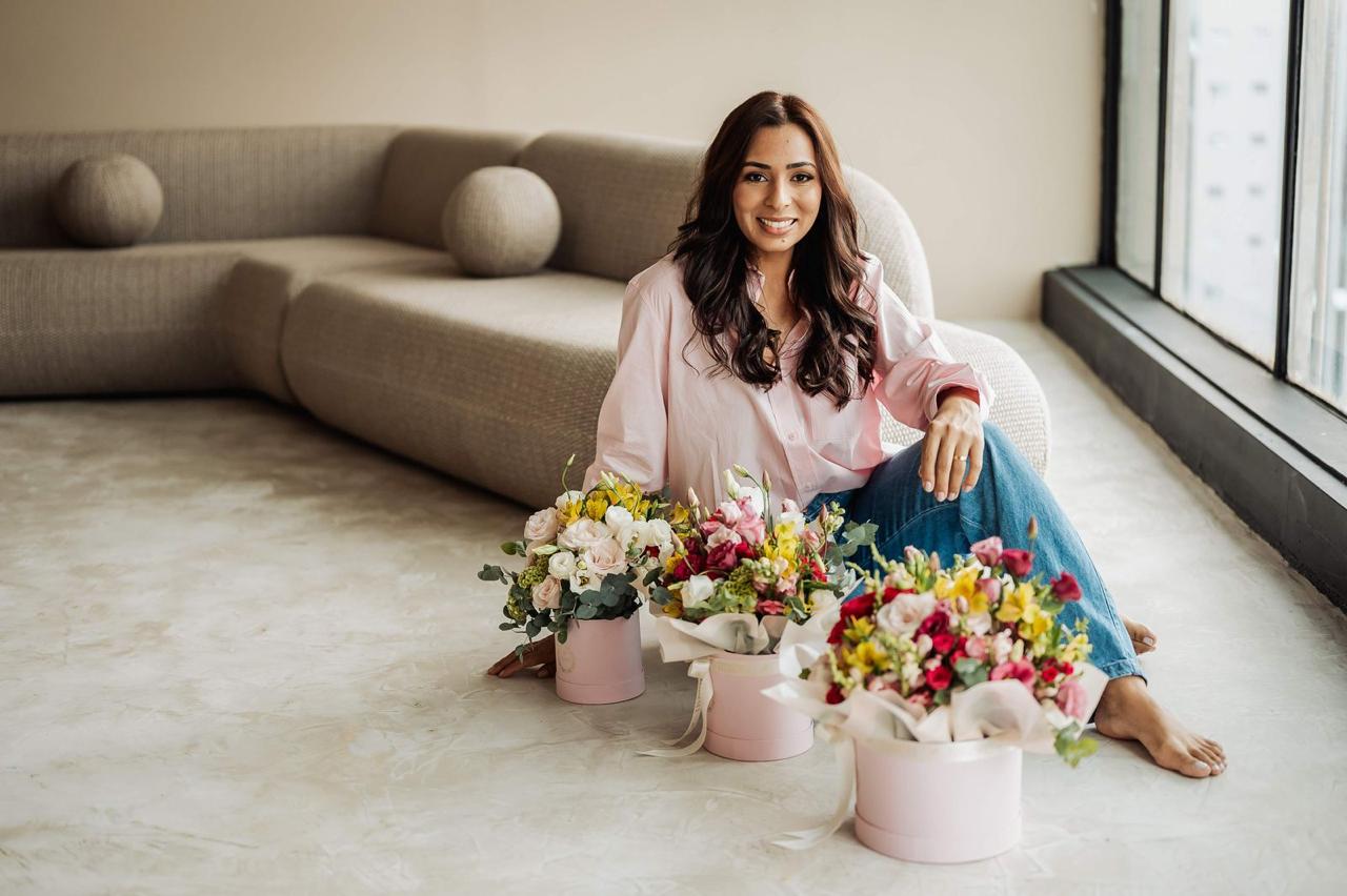 Rosellis Lucena sentada ao lado de boxes florais no ateliê da La Vie Fleurie